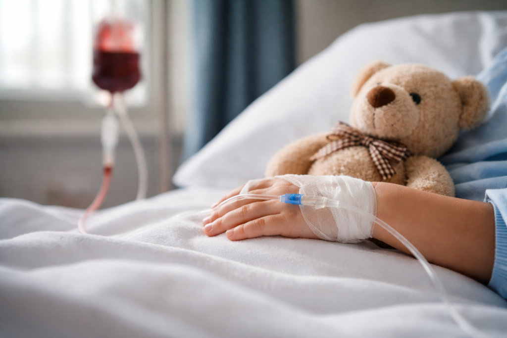 Kinderhand im Krankenhausbett mit Infusion und Teddybär als Symbol für medizinische Entscheidungen bei Minderjährigen